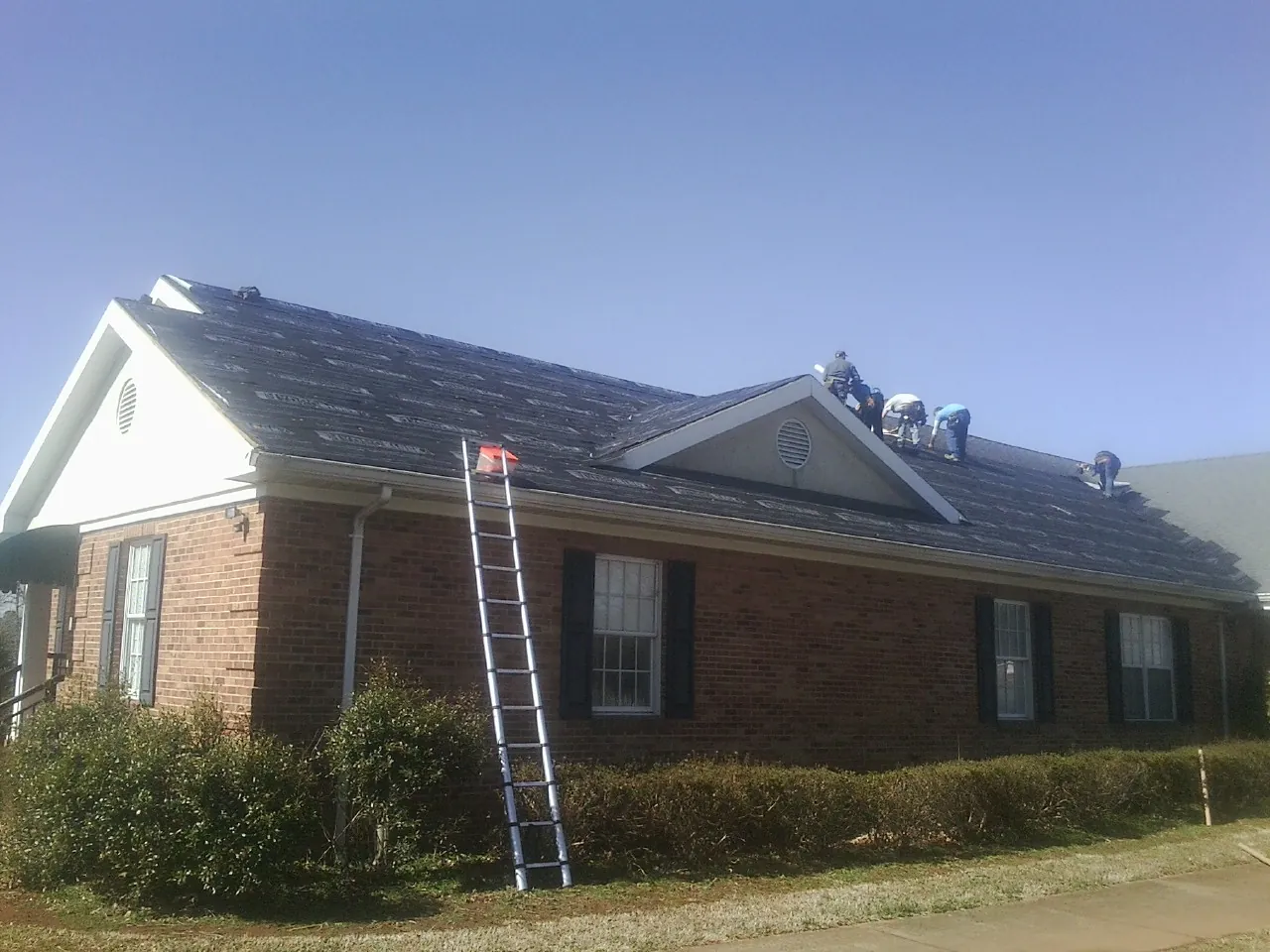 Crew tearing shingles off a brick ranch roof with a ladder set — Metal Roof Repair work by our crew in Woolford