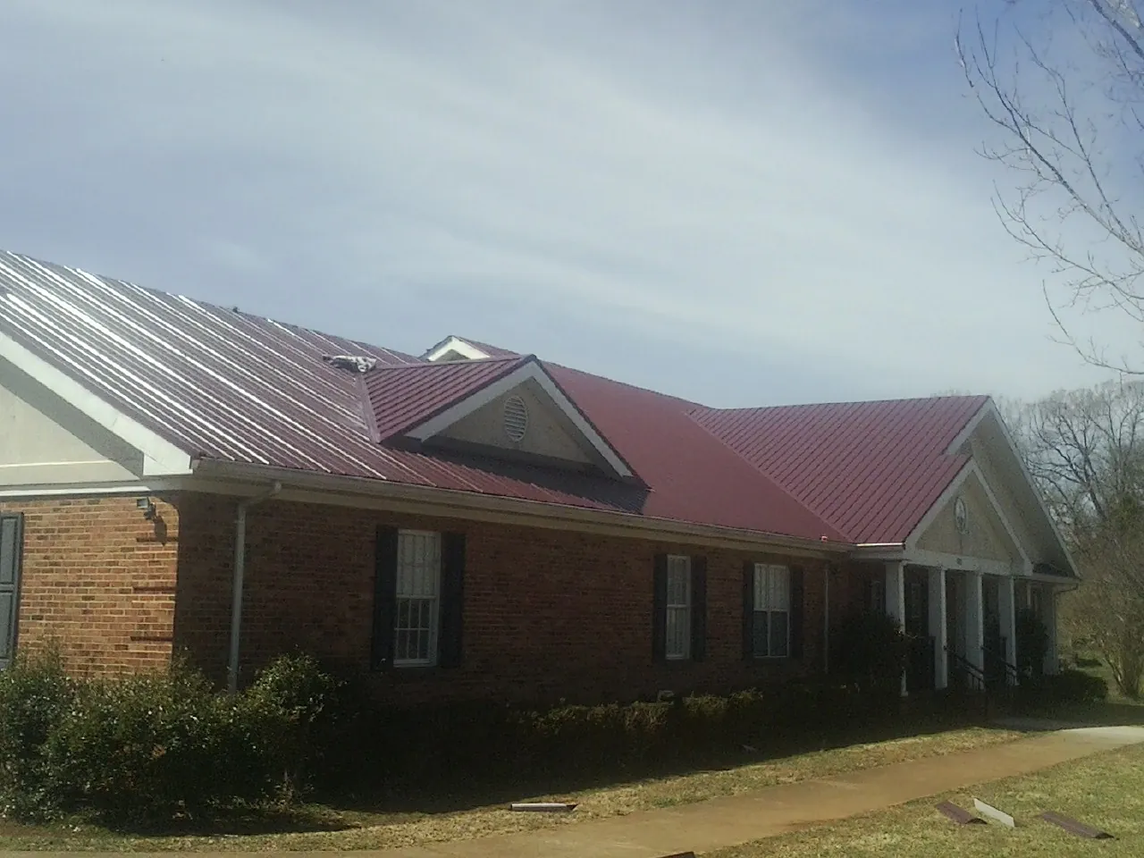 Red metal roof with gabled entries on a long brick building, from a Hail Damage Roof Repair job in Woolford