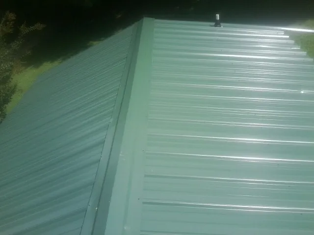 New green metal panels meeting at the ridge of a roof — Flat Roof Repair work by our crew in Woolford