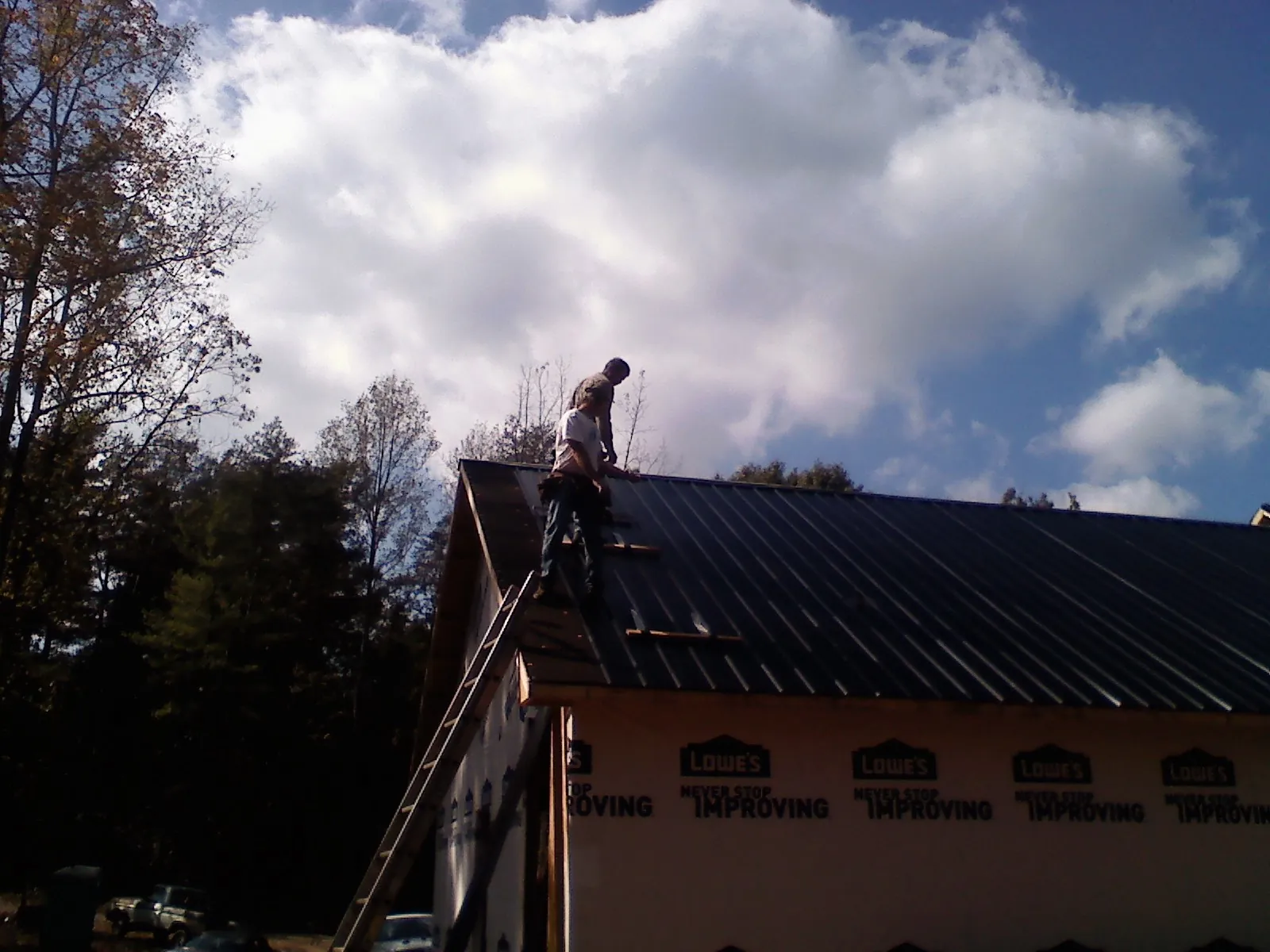Roofer fastening dark metal panels high against a cloudy sky, from a Roof Inspection job in Woolford