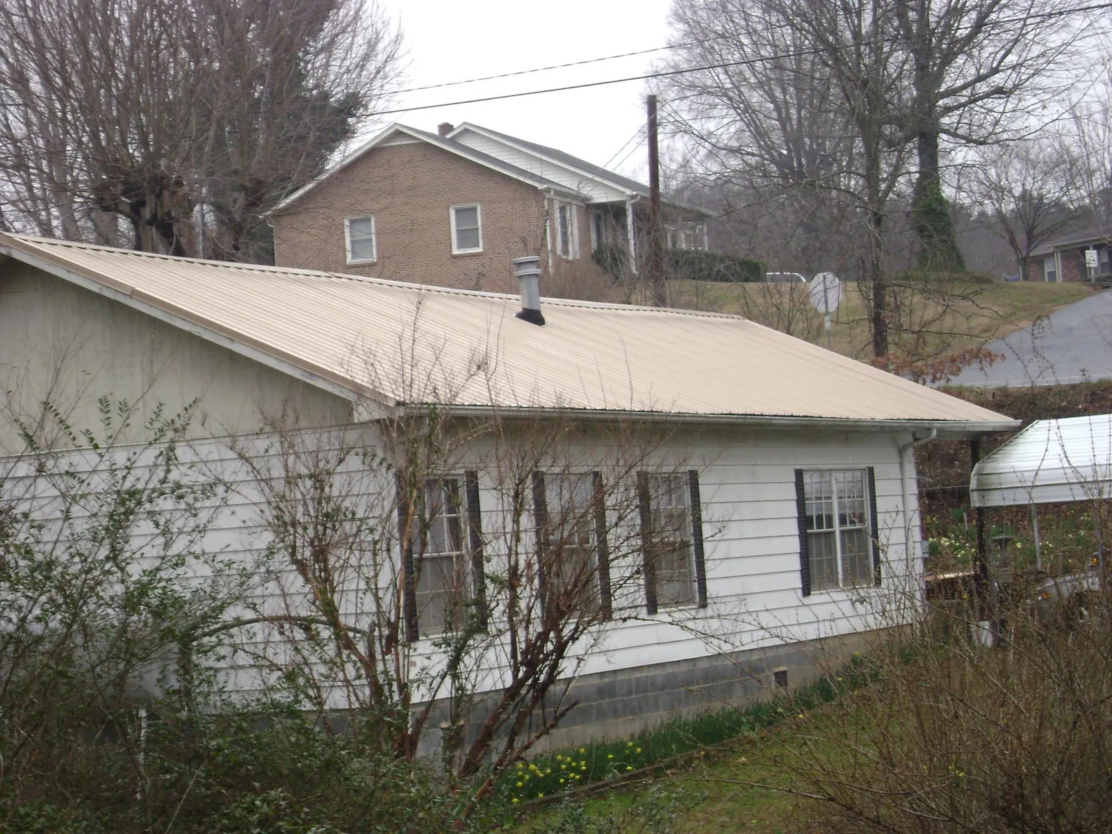 Tan metal roof on a white sided house set into a hillside — Commercial Roofing by Roofing Brothers in Woolford