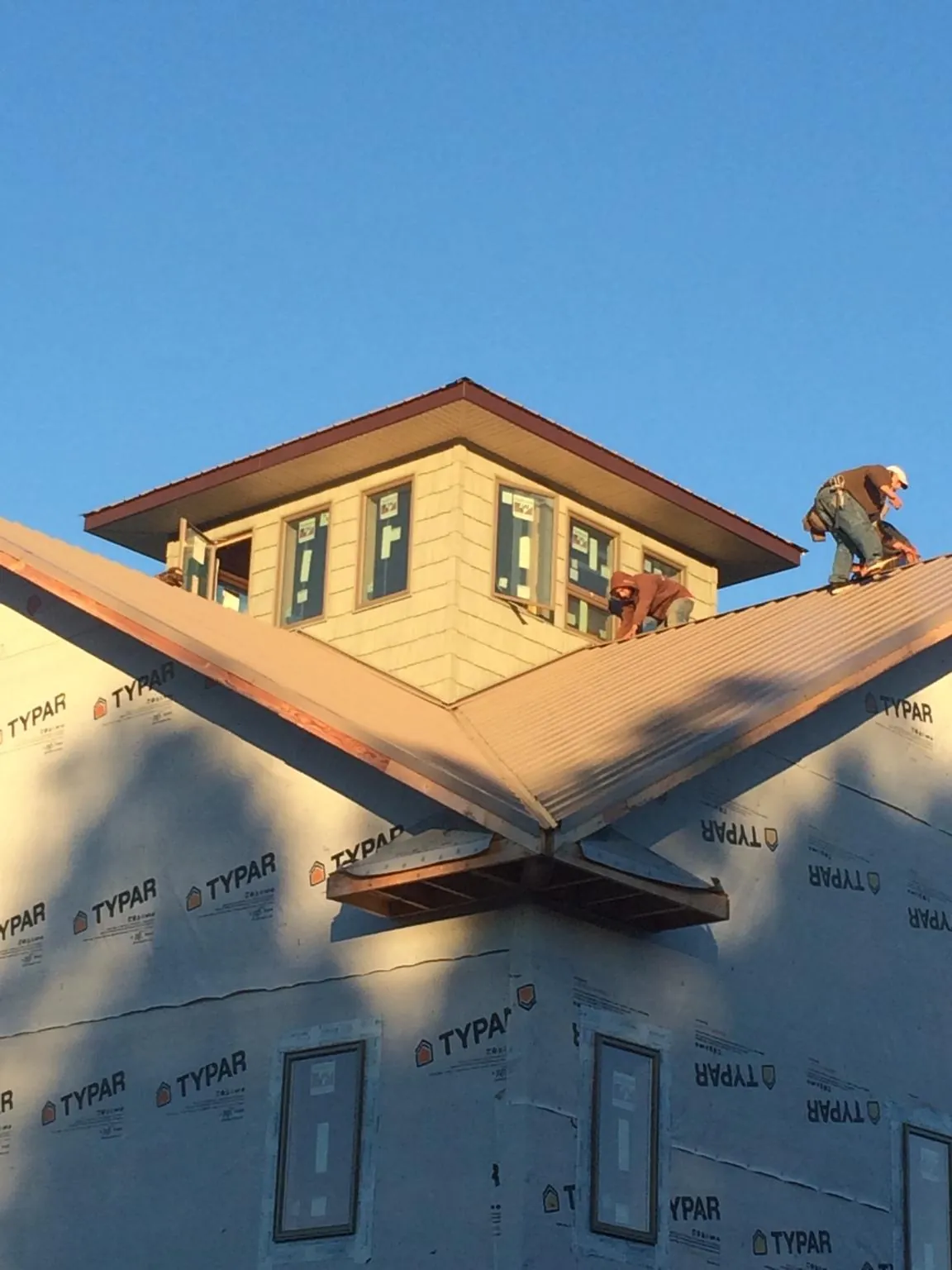 Roofers working around a rooftop cupola on a new metal roof at sunset — Roof Waterproofing in Woolford by Roofing Brothers